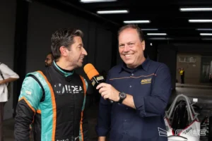 Piloto de Fórmula Vee sendo entrevistado nos boxes do autódromo após atividade em pista, com microfone e equipe ao fundo