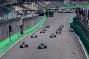 Carros da Fórmula Vee alinhados e acelerando na reta principal do Autódromo de Interlagos durante o momento da largada, com pilotos disputando posições nos primeiros metros da corrida.