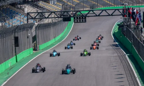 Carros da Fórmula Vee alinhados e acelerando na reta principal do Autódromo de Interlagos durante o momento da largada, com pilotos disputando posições nos primeiros metros da corrida.